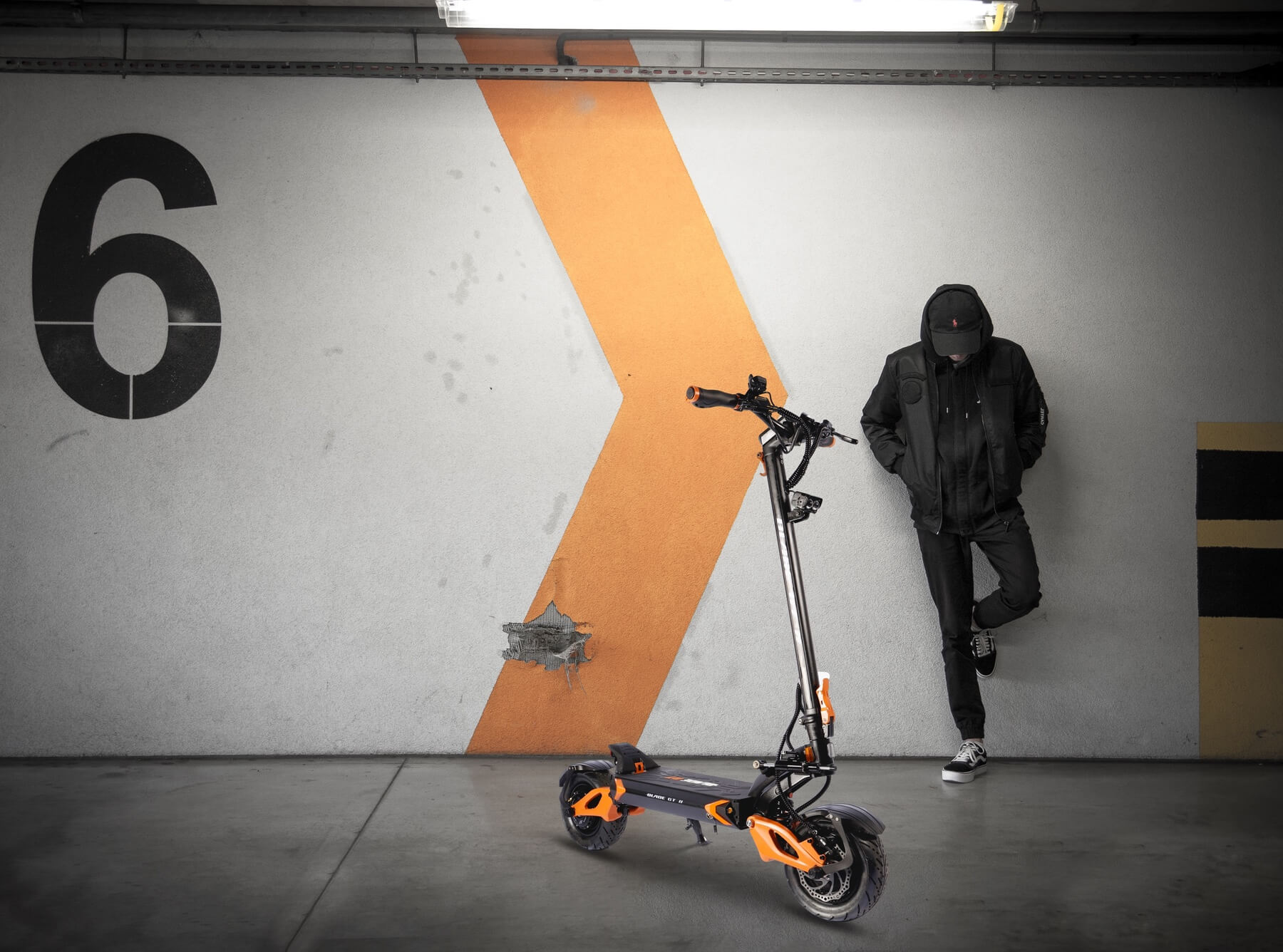 A man standing next to a Blade GT+ II scooter in a garage.